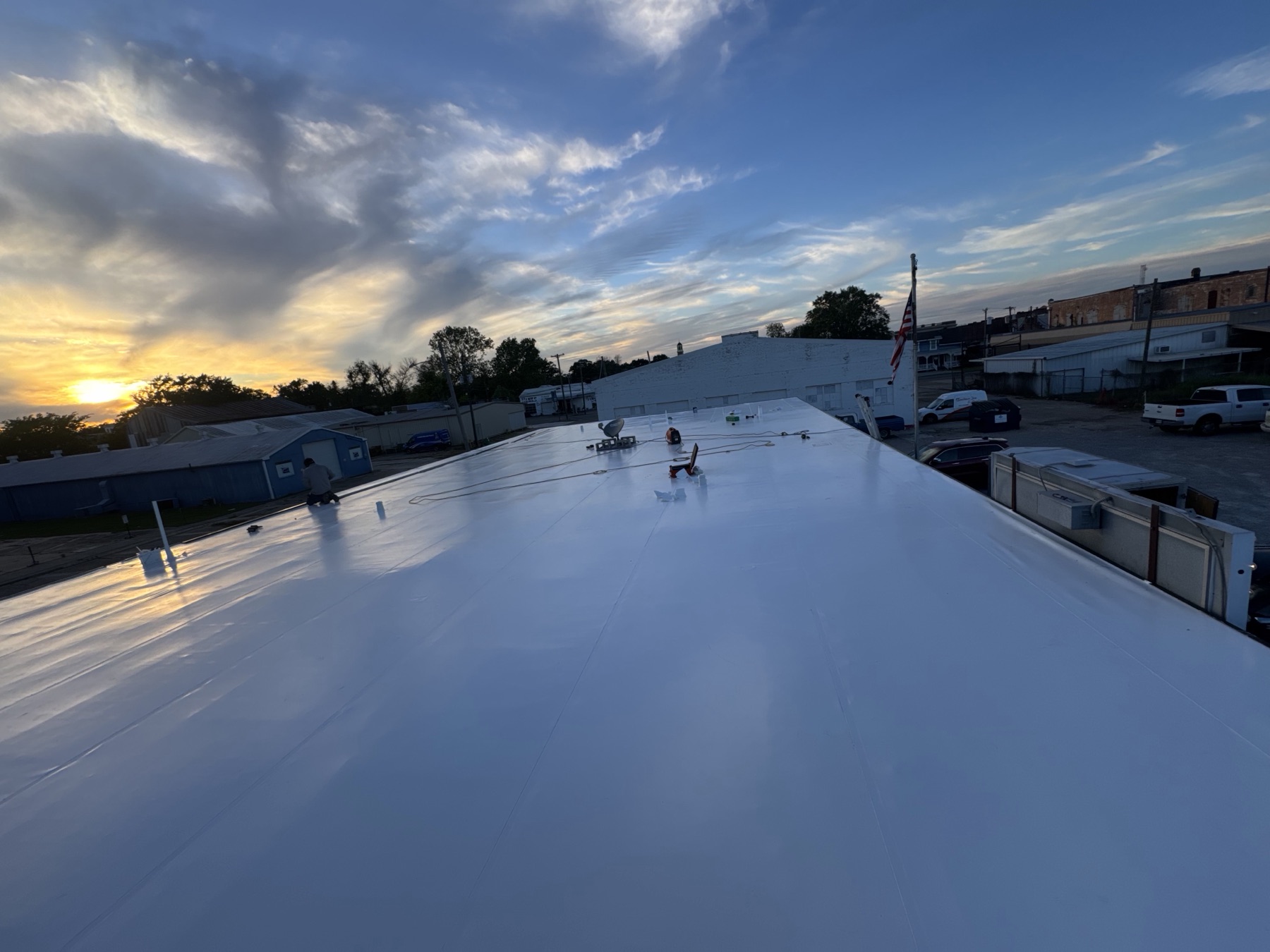 Crowley Louisiana commercial TPO roof replacement by Bayou Roofing — completed white fully-adhered TPO membrane photographed at sunset with American flag and downtown buildings visible