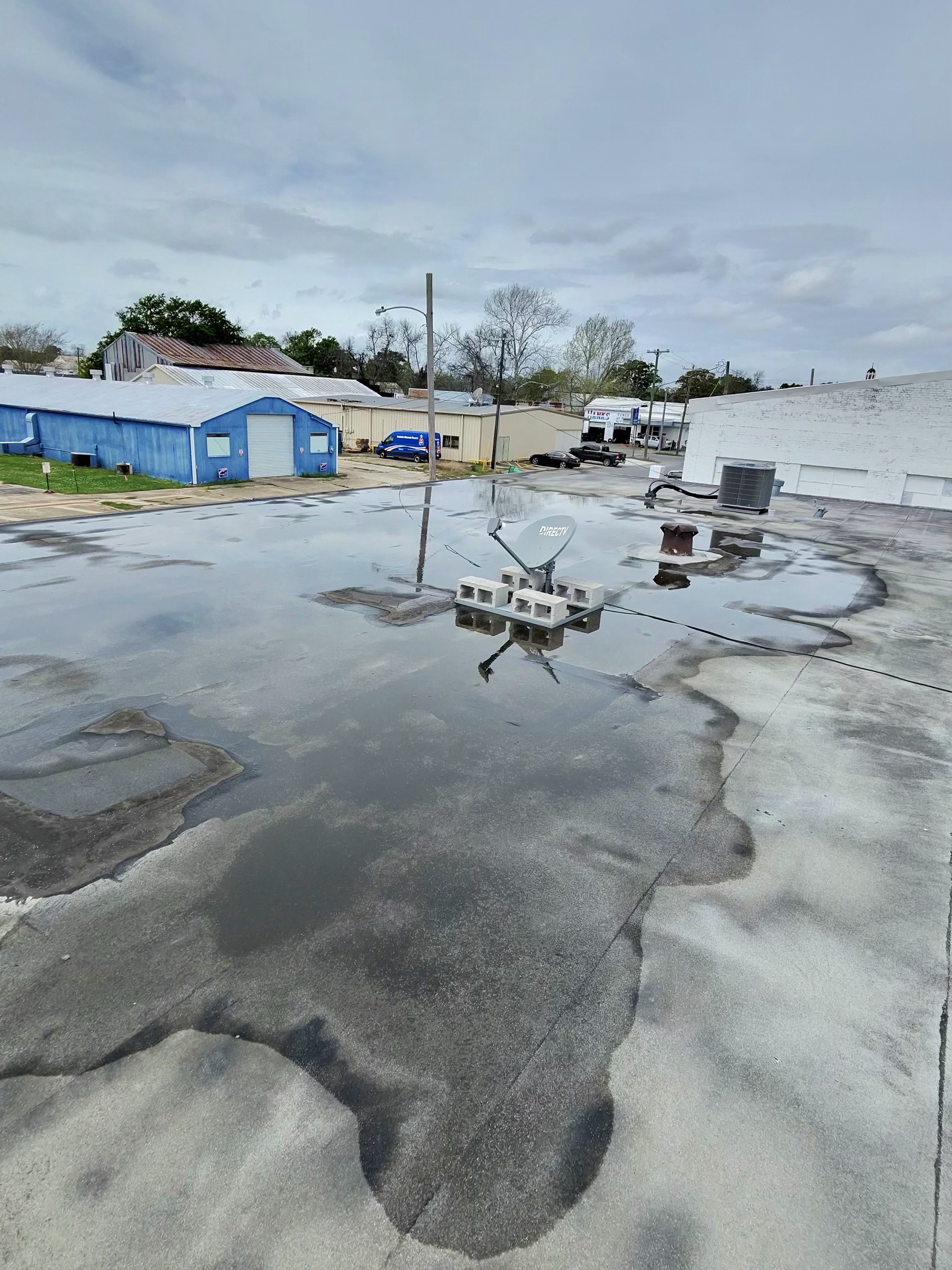 Aerial view of the aging commercial flat roof in Crowley, Louisiana before TPO replacement, showing significant ponding water and a satellite dish weighted with cinder blocks.